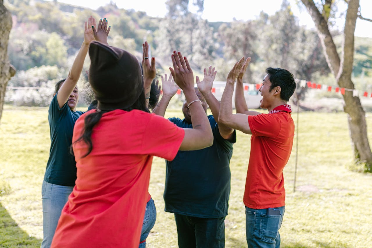 Diverse friends in park high-fiving during fun team-building exercise.