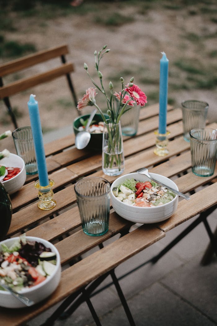 A beautifully set outdoor table with healthy salads, candles, and flowers creating a serene dining atmosphere.